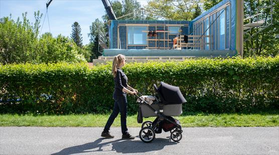 Fotografi om en kvinna med barnvagn som går förbi ett hus som håller på att byggas.